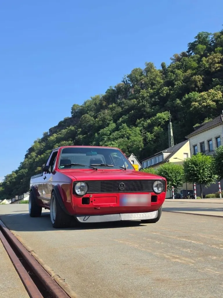Roter VW Golf Caddy Youngtimer vor bewaldetem Hang